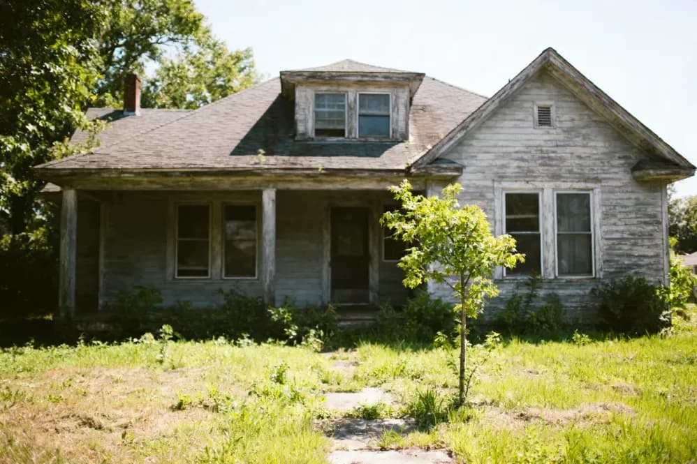 Vacant Iowa house with an overgrown lot, the kind of empty property that costs money to hold.
