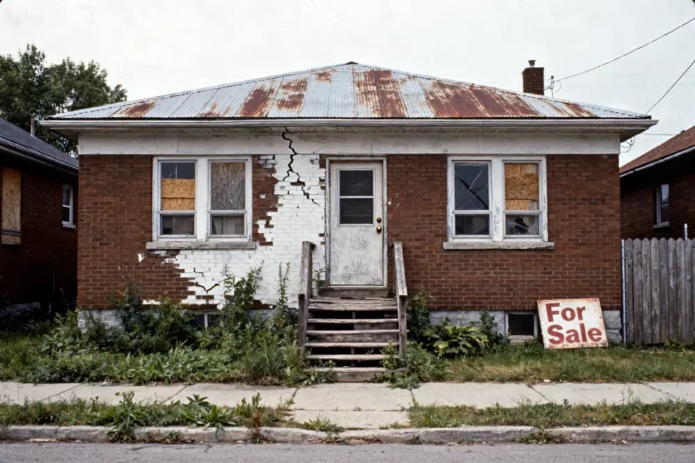 Iowa house with a for-sale sign and overgrown yard, typical of a property sold ahead of a foreclosure sale date.